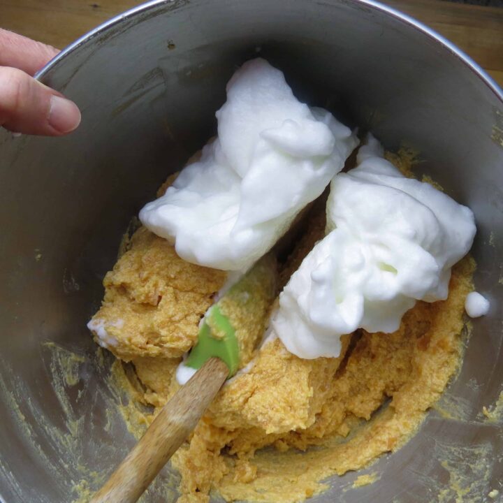 A mixing bowl with a spatula folding egg whites into a batter.