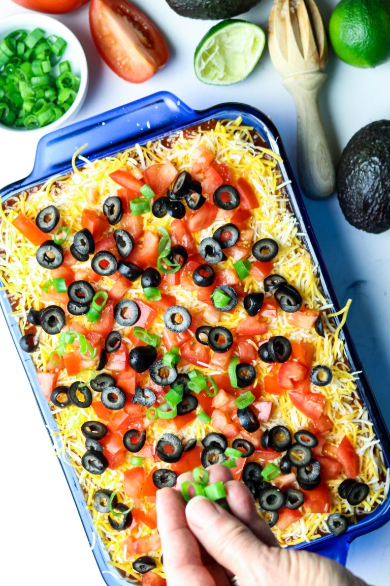 A blue casserole dish filled with Baked Mexican Layered Dip.