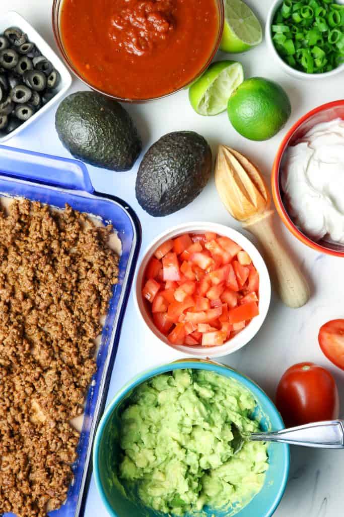 Ingredients of avocado, tomatoes, sour cream and taco meat for a baked dip.