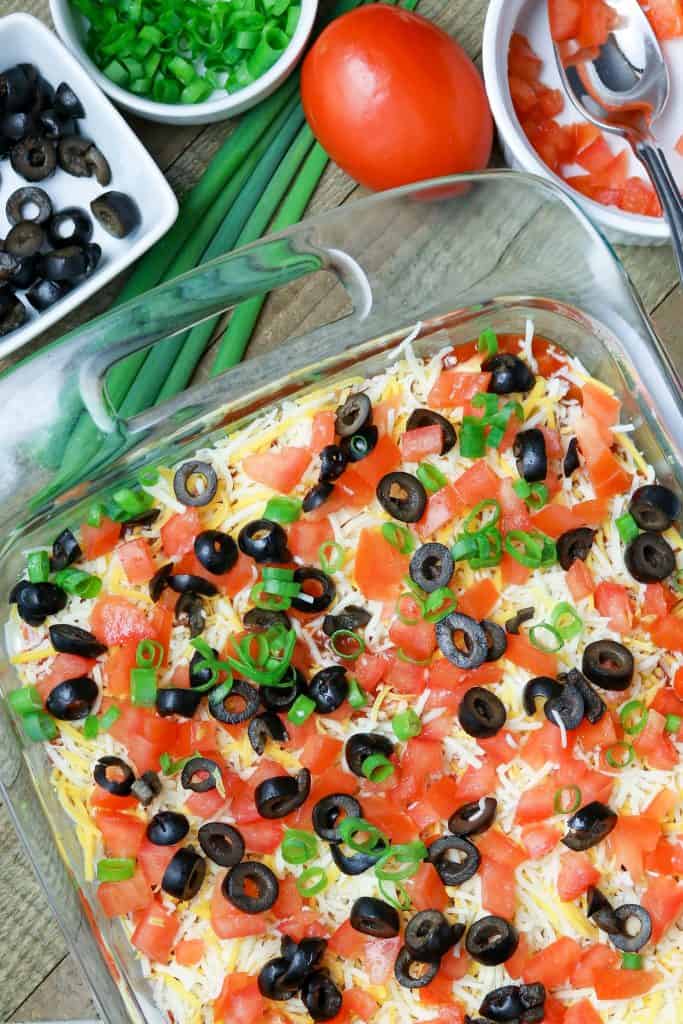 A dish of Baked Mexican Layered Dip with ingredients scattered about.