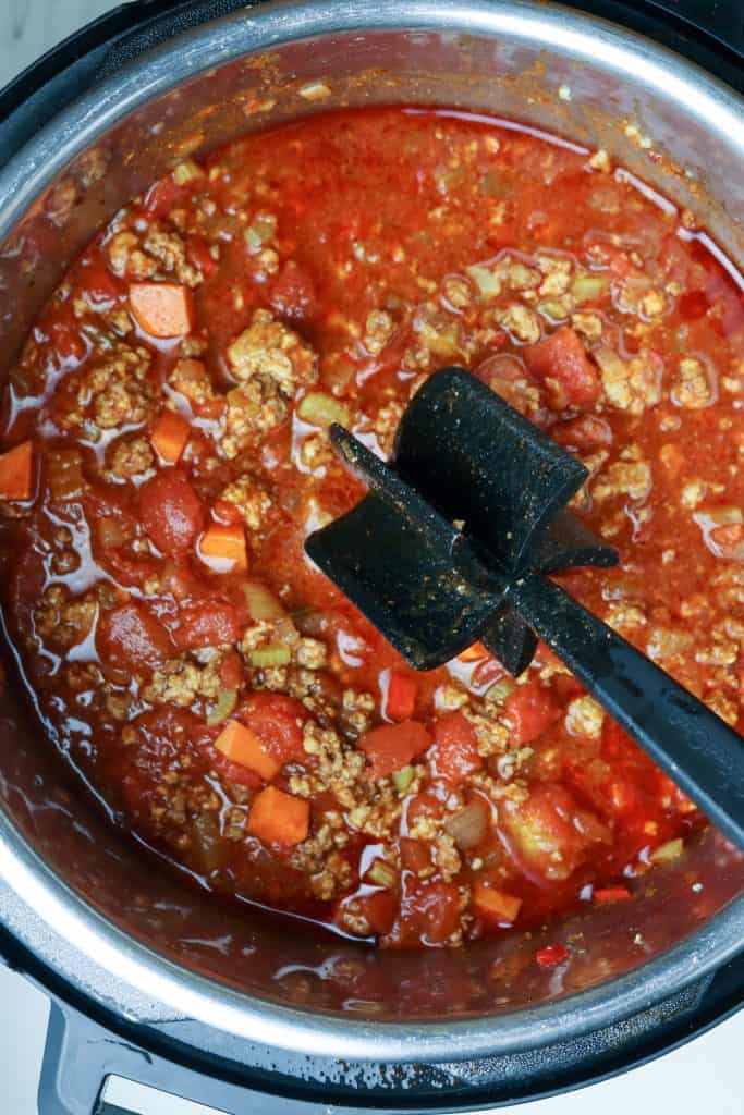 A pot of chili in a pot with a chopping spoon.