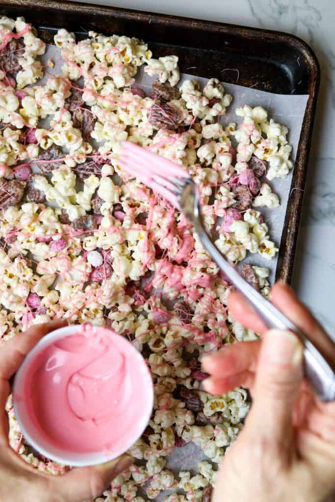 Drizzling pink icing on popcorn, nuts and candy.