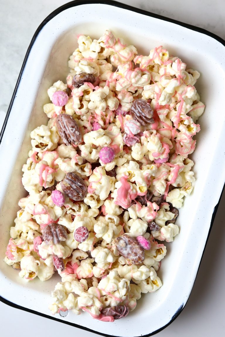 A pan of popcorn with nuts and candy covered chocolates.