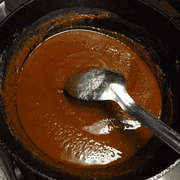 A black pot with a dark roux and a silver spoon in it.