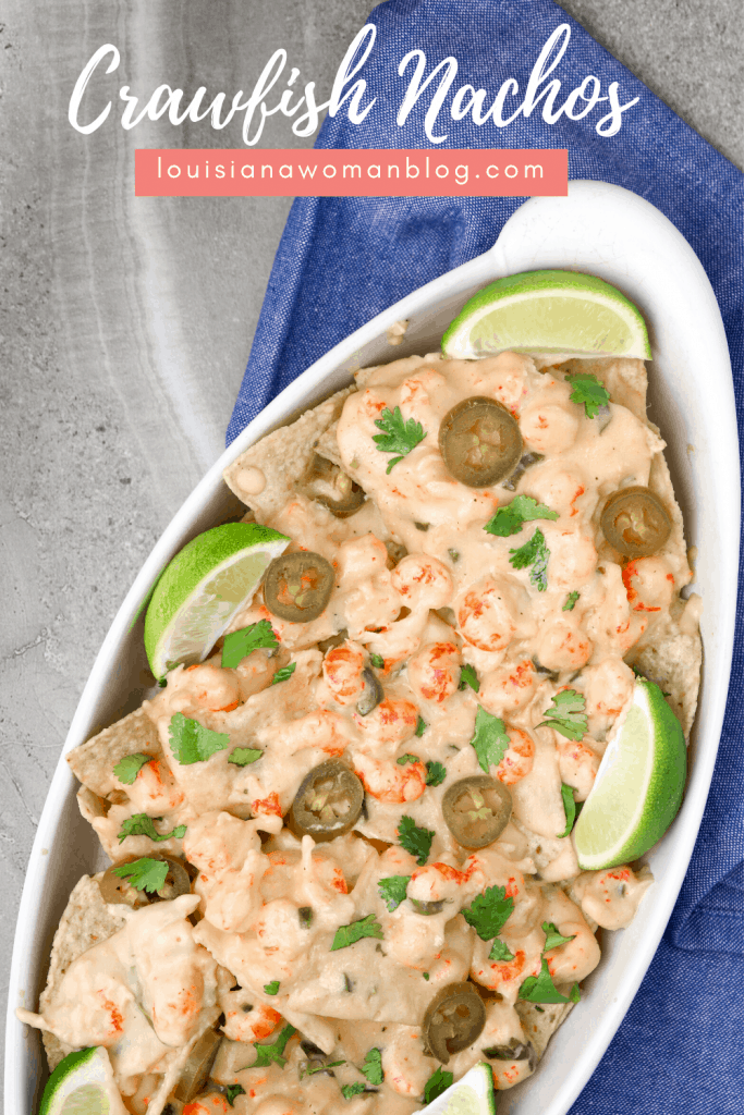 A dish of cheesy crawfish dip on top of tortilla chips with lime slices.