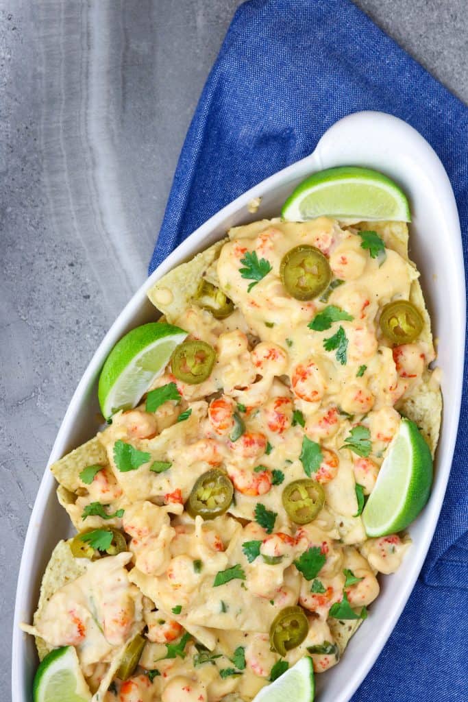 A dish of cheesy crawfish dip on top of tortilla chips with lime slices for Mardi Gras Food Recipes.