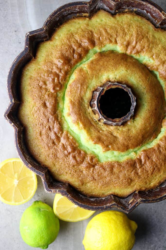 A baked cake in a bundt pan with fresh lemons and limes beside it.