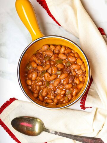 Saucy Pork And Beans in a crock with a serving spoon.