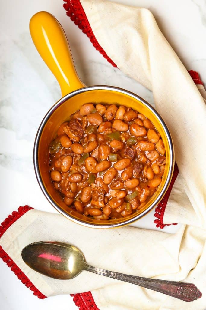 Saucy Pork And Beans in a crock with a serving spoon.