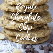 A stack of chocolate chip cookies with chocolate chips and coconut flakes beside it.