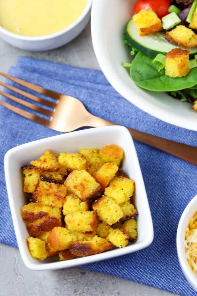 A bowl of cornbread croutons next to a salad.