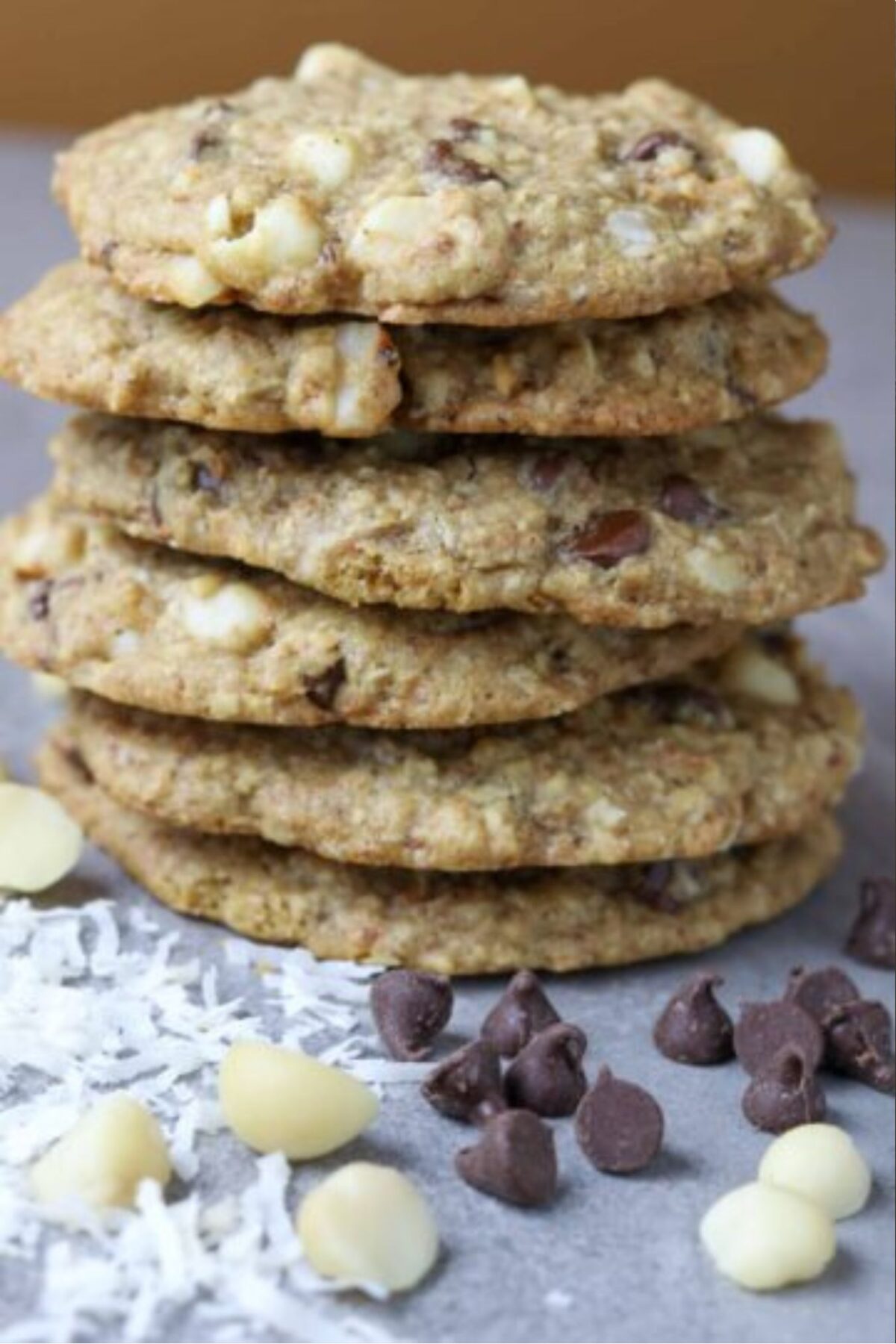 A stack of chocolate chip cookies with chocolate chips and coconut flakes beside it.