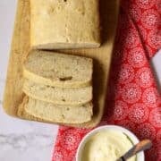 A sliced loaf of banana bread on a red and white napkin next to a bowl of butter.
