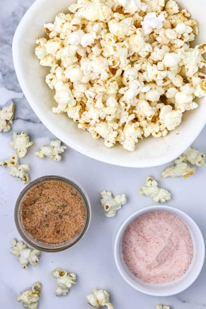 A bowl of popcorn and two containers of seasonings.