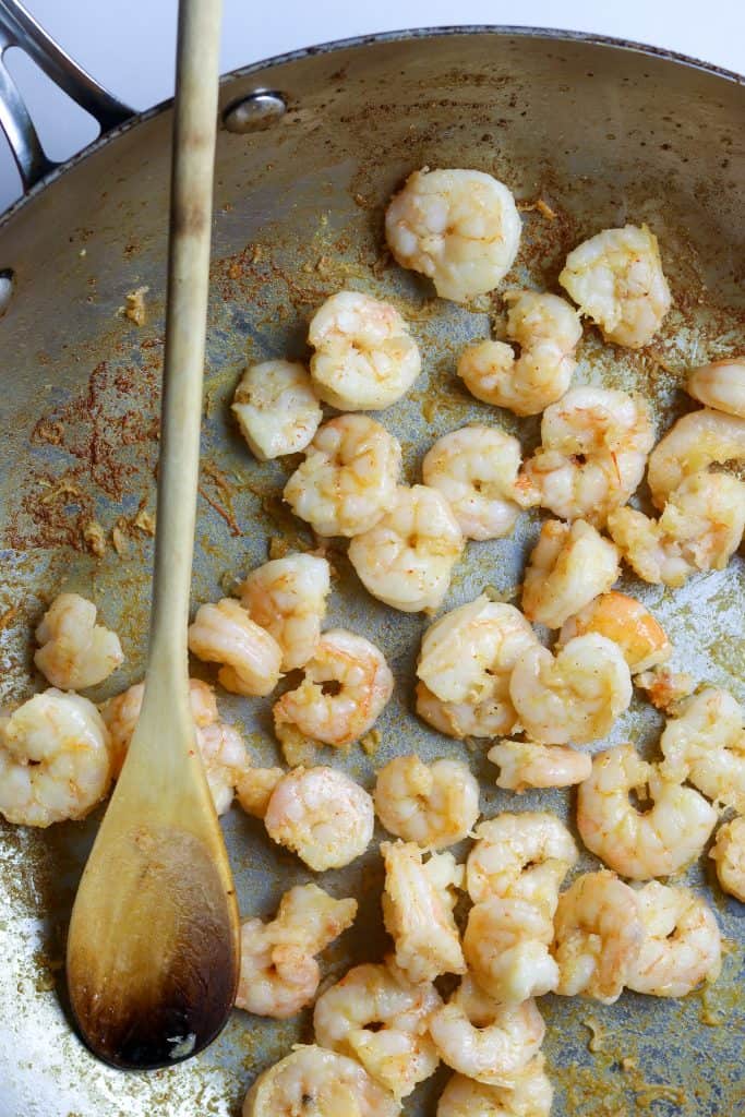 A pan of sautéed shrimp with a wooden spoon.