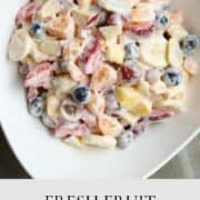 A white salad bowl filled with a creamy fruit salad.