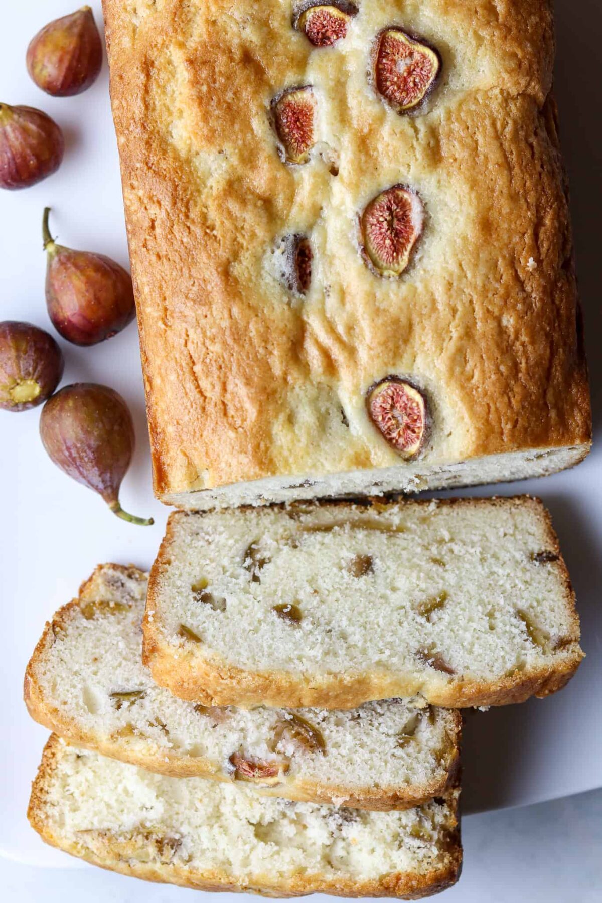 A sliced loaf of fresh fig bread laying next to fresh figs.