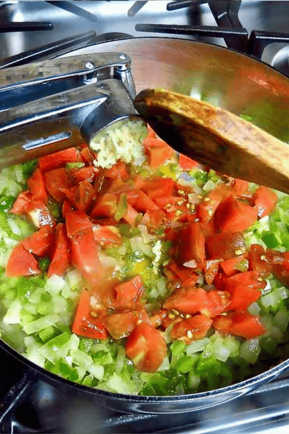 A pot of tomatoes, and the Cajun trinity with pressed garlic added with a wooden spoon.