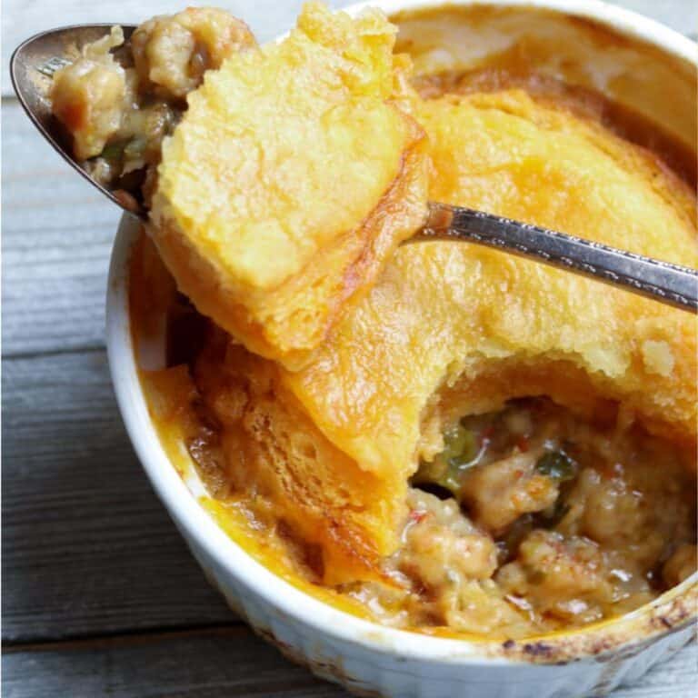 A round white individual baking dish with a spoonful of crawfish pot pie resting on the bowl rim over the crust.