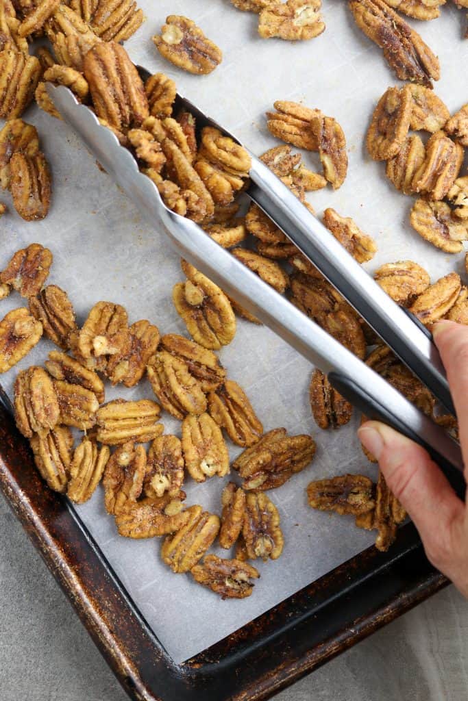 Tossing roasted pecans with tongs.