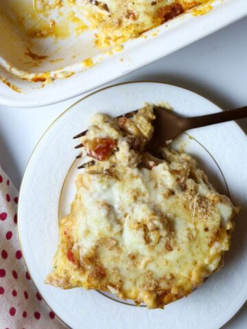 A plate of lasagna with a forkful and a casserole dish of lasagna.