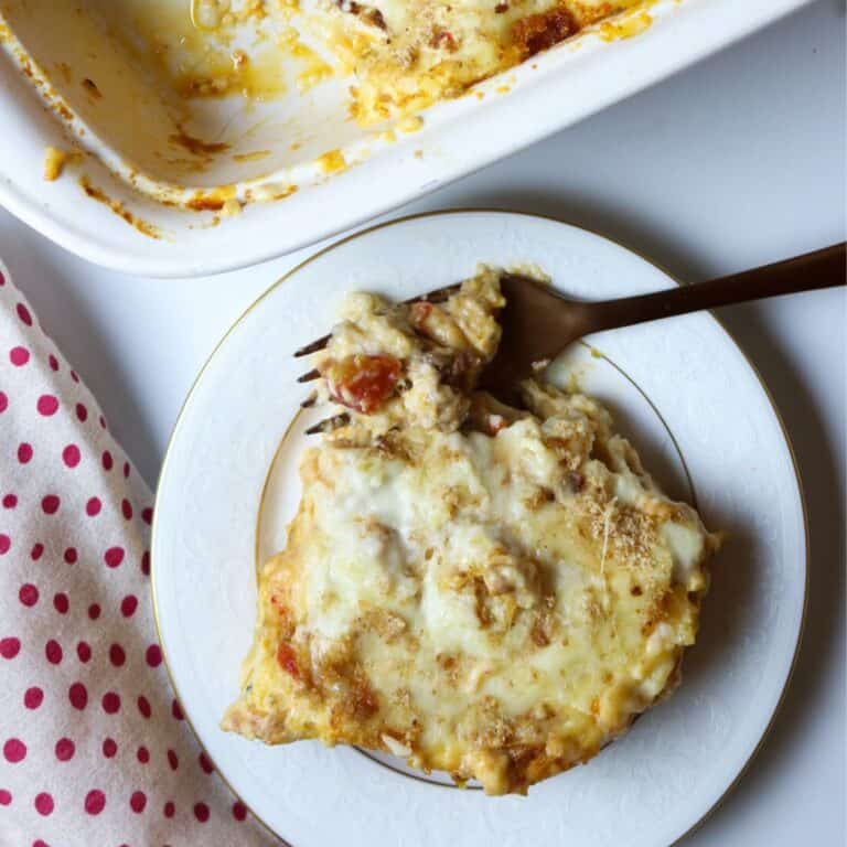 A white plate of cheesy crawfish lasagna with a fork next to a casserole dish.