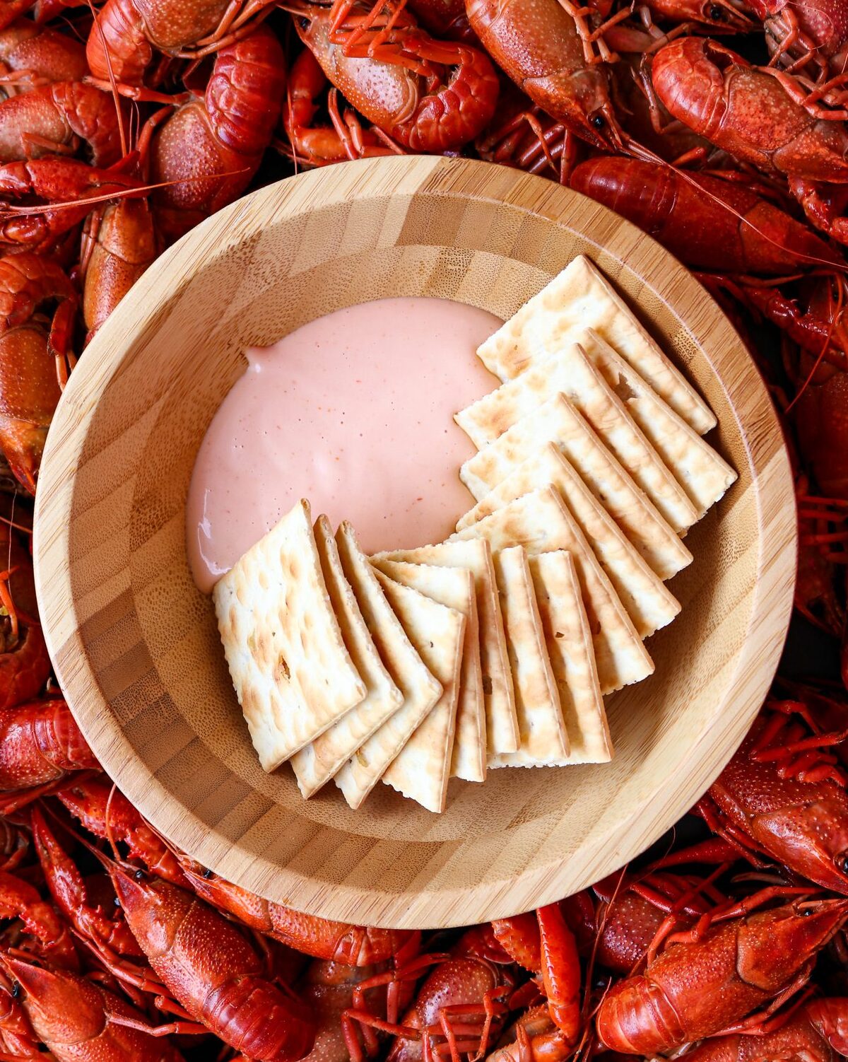 Bowl with dip and crackers in a pan of crawfish.