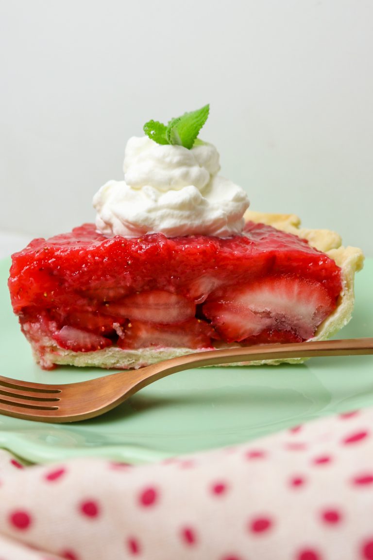 Slice of strawberry pie with a dollop of whipped cream on top.