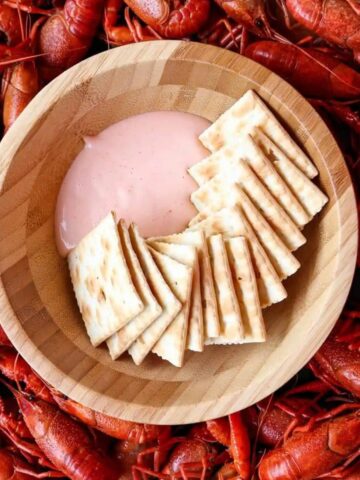 A bowl of dip with saltines sitting on a platter of crawfish.