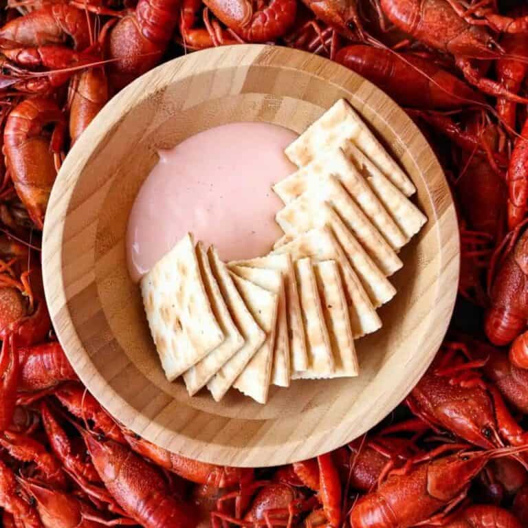 A pile of crawfish with a wooden bowl of sauce and crackers.