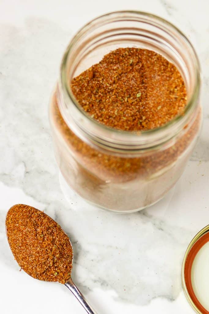 A jar of taco seasoning with a spoonful beside it.