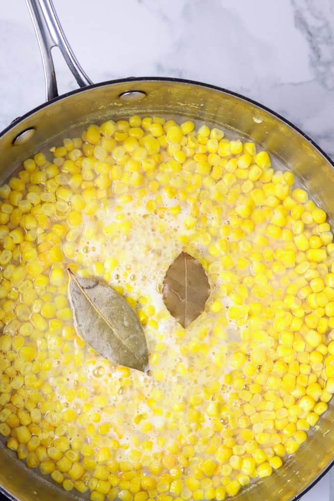 Corn cooking in a pan with bay leaves.
