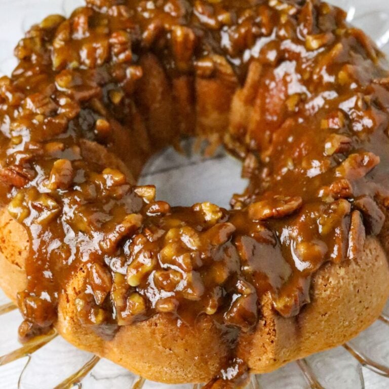 A bundt cake with a pecan caramel glaze on top on a glass cake plate.