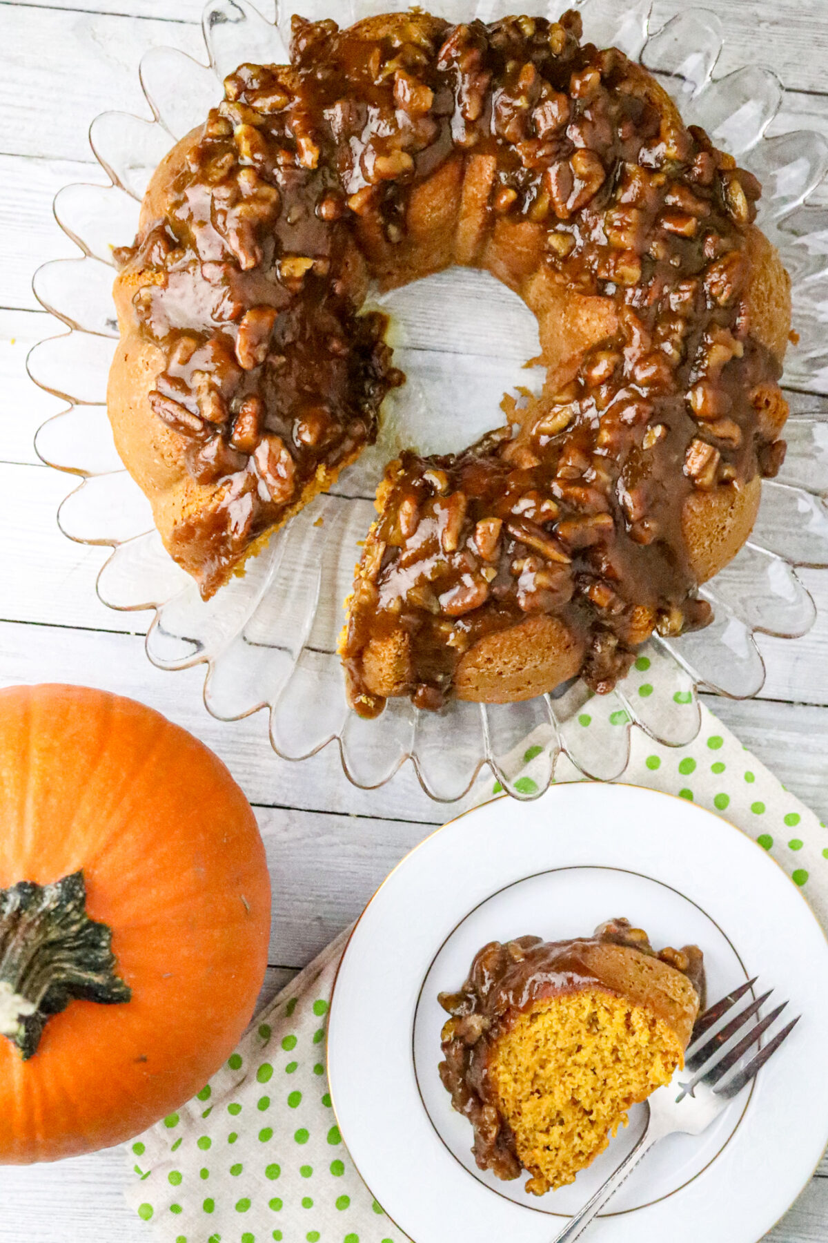 A mini pumpkin next to a slice of 2-Ingredient Pumpkin Cake With Brown Sugar Glaze on a plate with a fork.