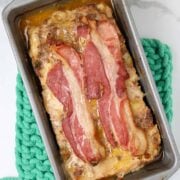 A cooked meatloaf in a loaf pan covered with bacon.