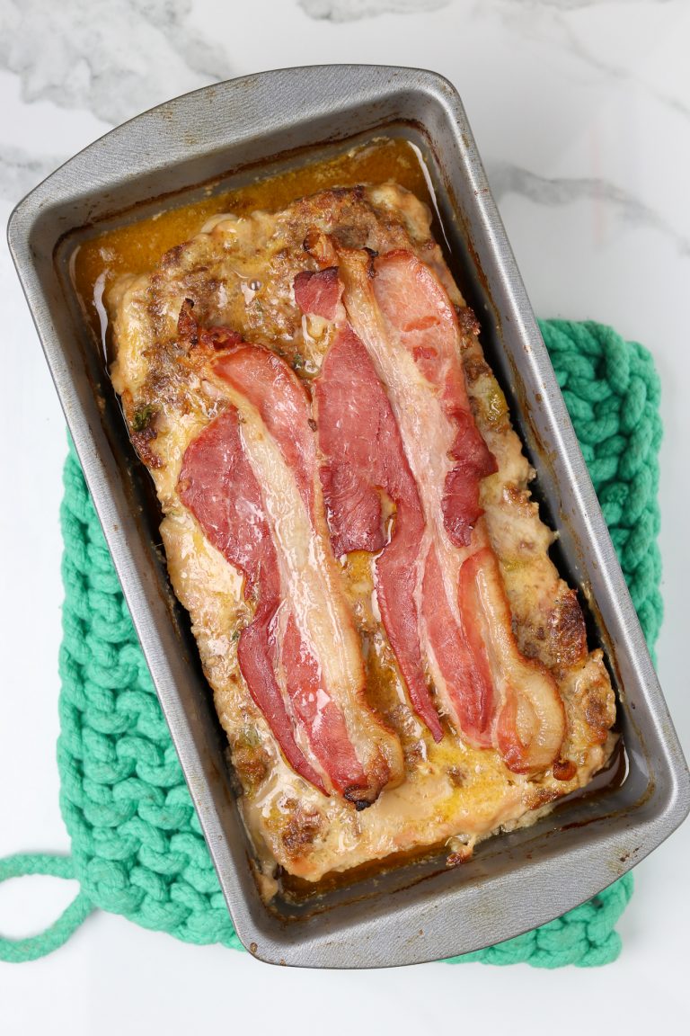 A cooked meatloaf in a loaf pan covered with bacon.