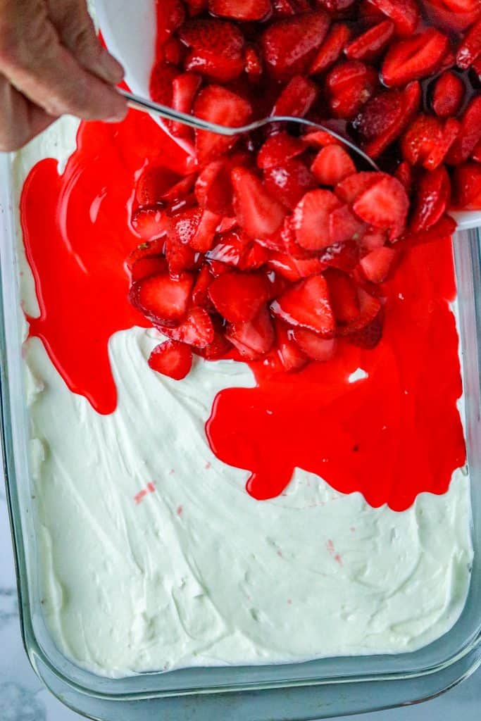 Strawberries poured onto a layer of cream cheese filling for a Strawberry Pretzel Salad.