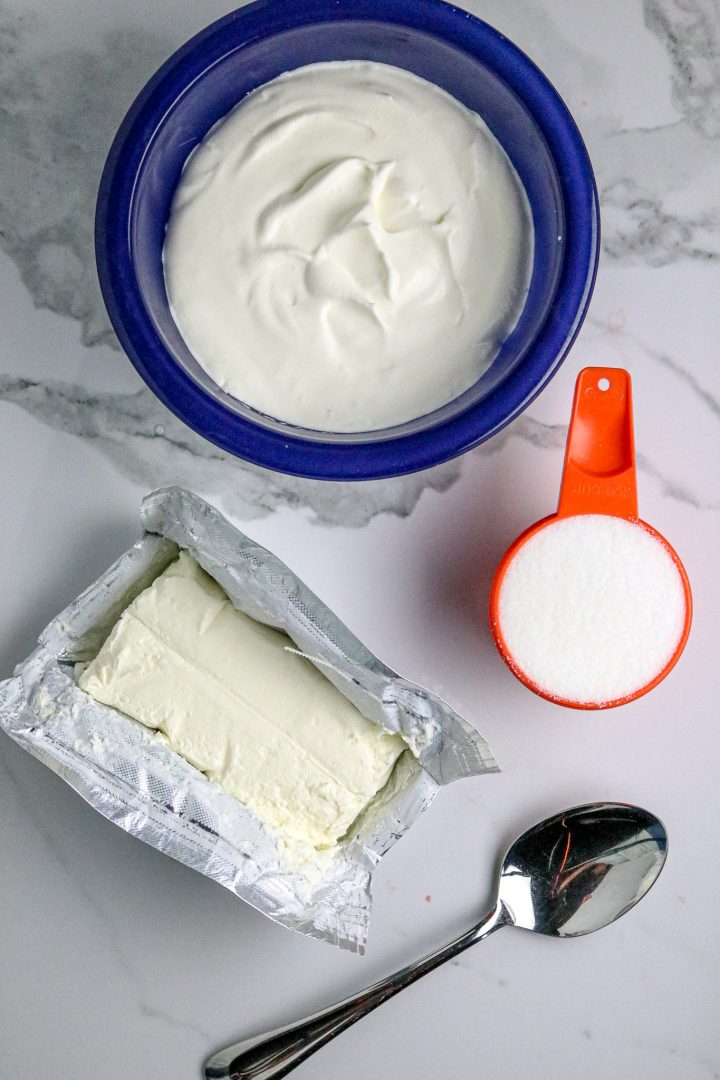 A bowl of whipped cream and a block of cream cheese with sugar in a measuring cup.