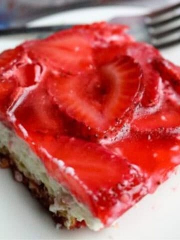 Photo of a pretzel crust dessert with strawberries on top on a plate with a fork.