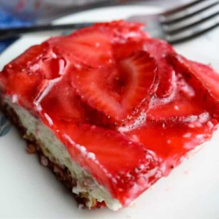 Photo of a pretzel crust dessert with strawberries on top on a plate with a fork.