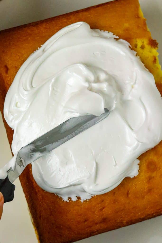 A spatula spreading frosting on Banana Pudding Cake Mix Cake.