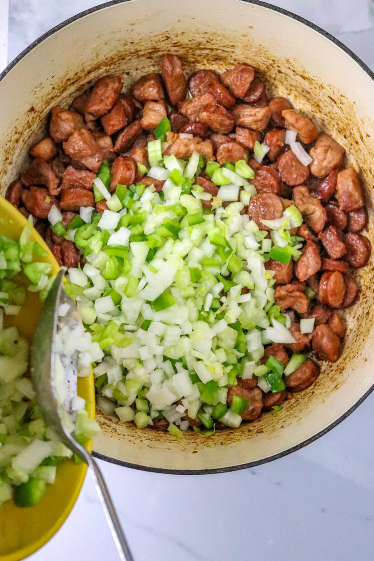 A pot of browned sausage and meat with chopped onions and peppers spooned into it.