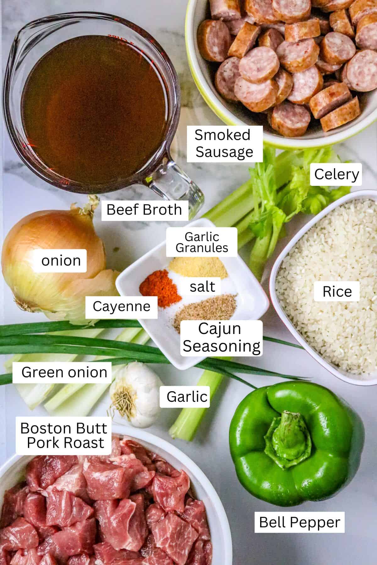 Ingredients of pork, sausage, vegetables, rice, and broth labeled on a white counter.