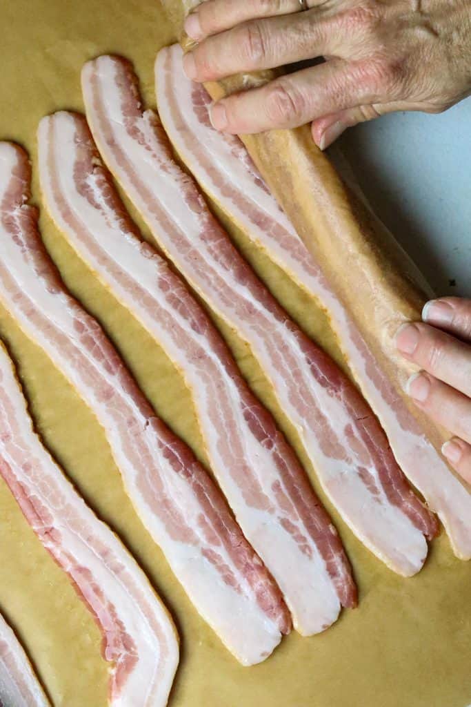 Strips of uncooked bacon rolled up on a parchment paper.