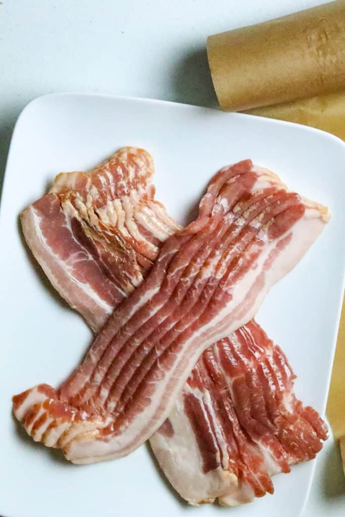 Uncooked bacon on a white plate.