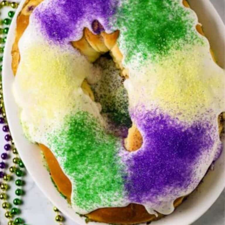 A round King cake with purple, yellow, and green icing. and beads around the bottom of the plate.