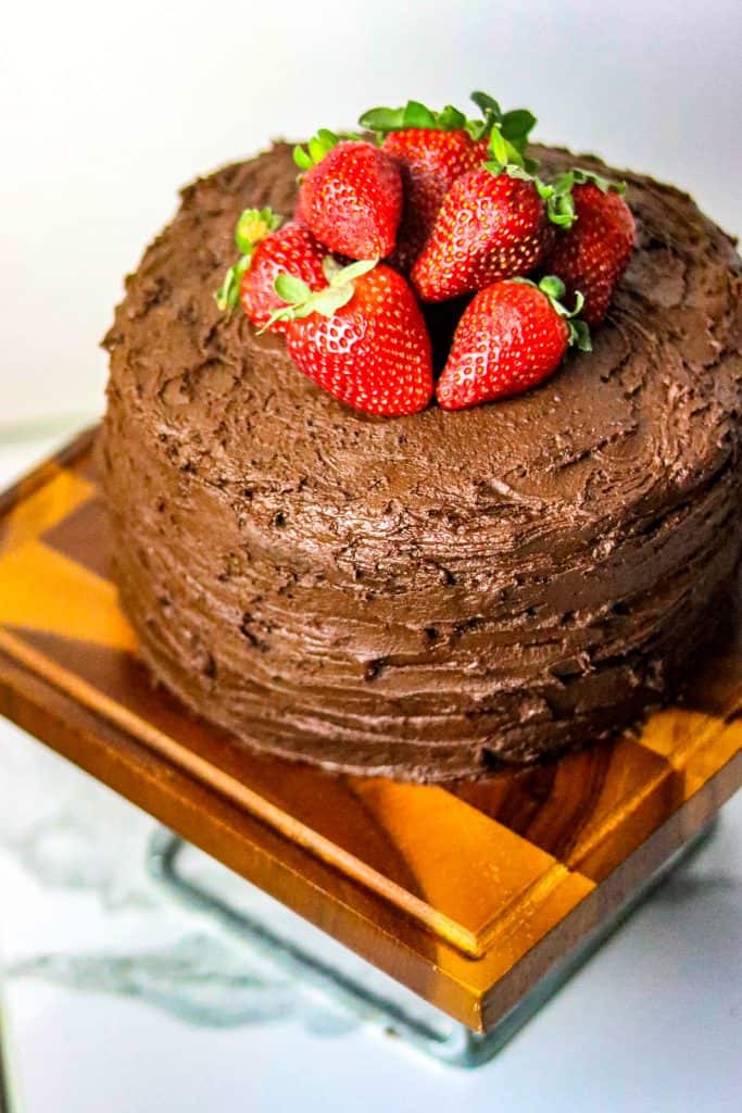 A chocolate cake on a wooden cake stand decorated with fresh strawberries,
