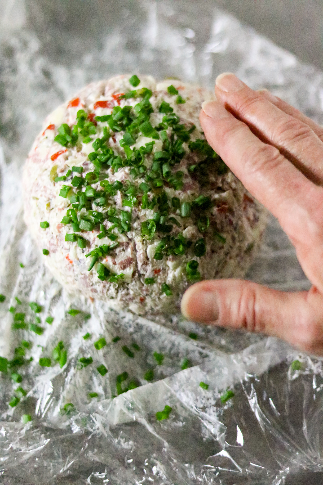 A hand patting a cheese ball with chopped chives.