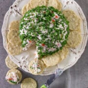 A cheese ball covered with chopped chives on a plate with crackers.