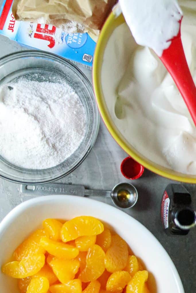 Ingredients pudding mix, mandarin oranges, and whipped cream in separate bowls.